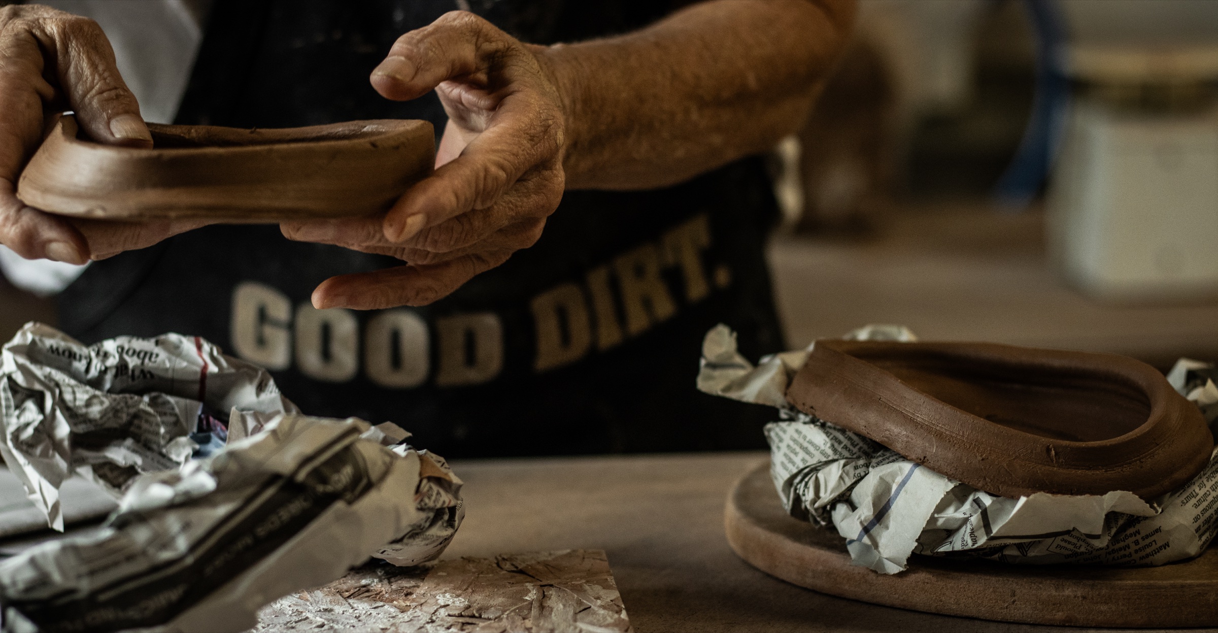 A ceramic artist examining a hand-built clay vessel beside another unfinished form
