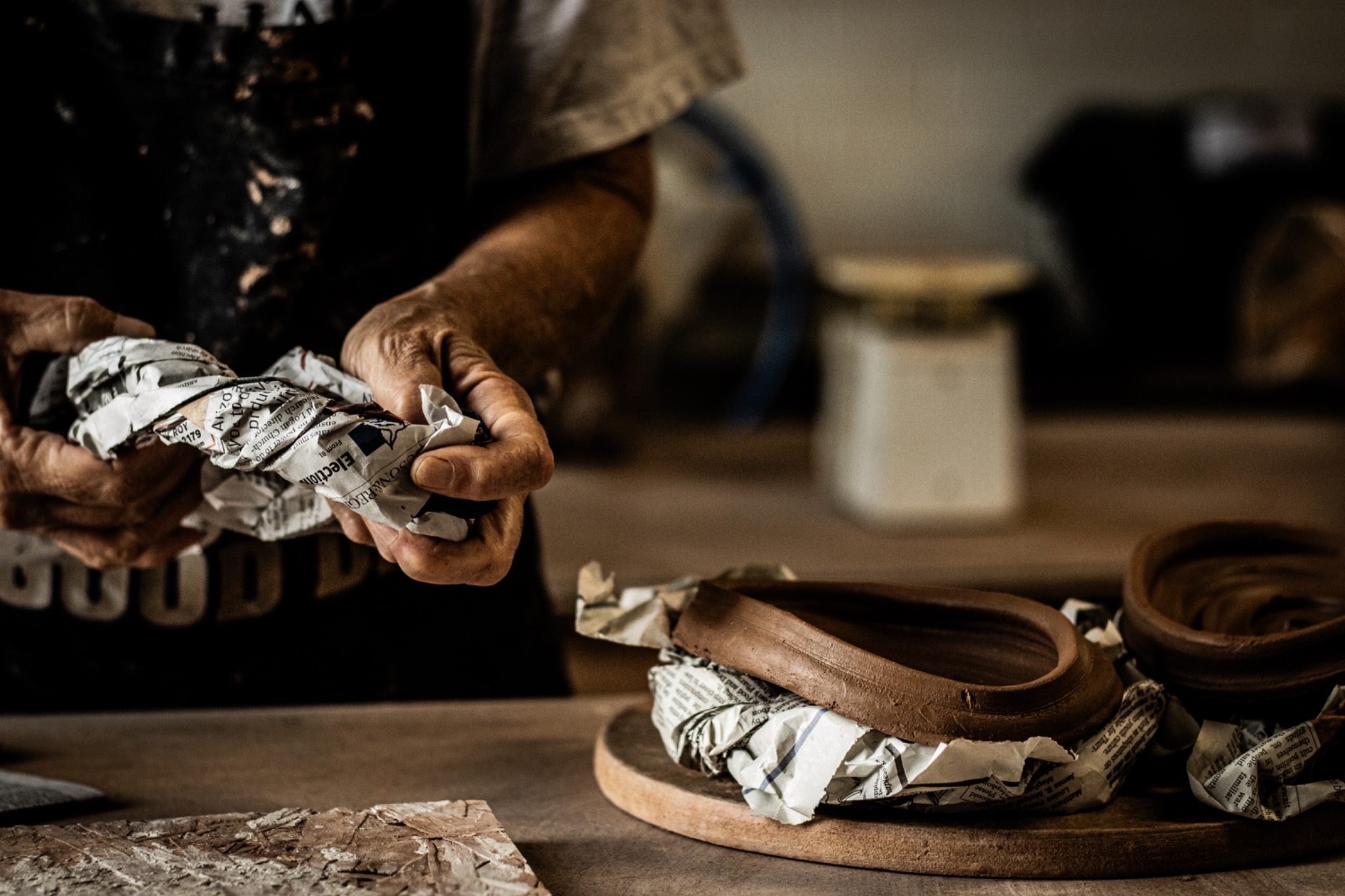 Hands wrapping handmade ceramics in newspaper