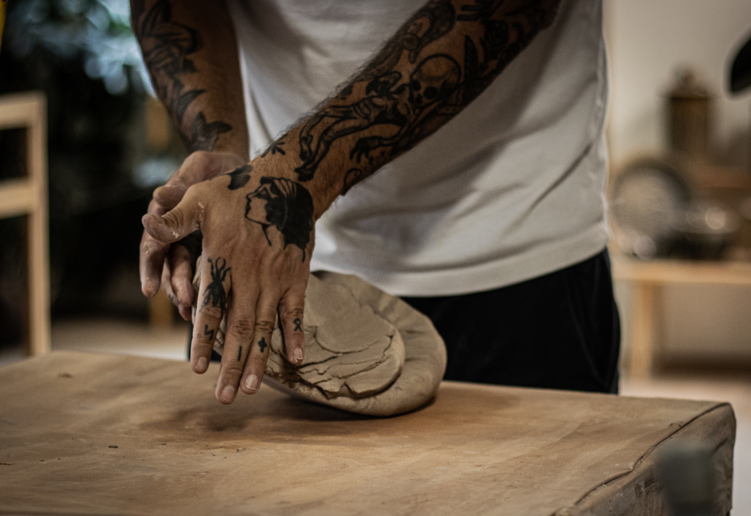 A tattooed ceramic artist pressing and shaping a large piece of clay by hand
