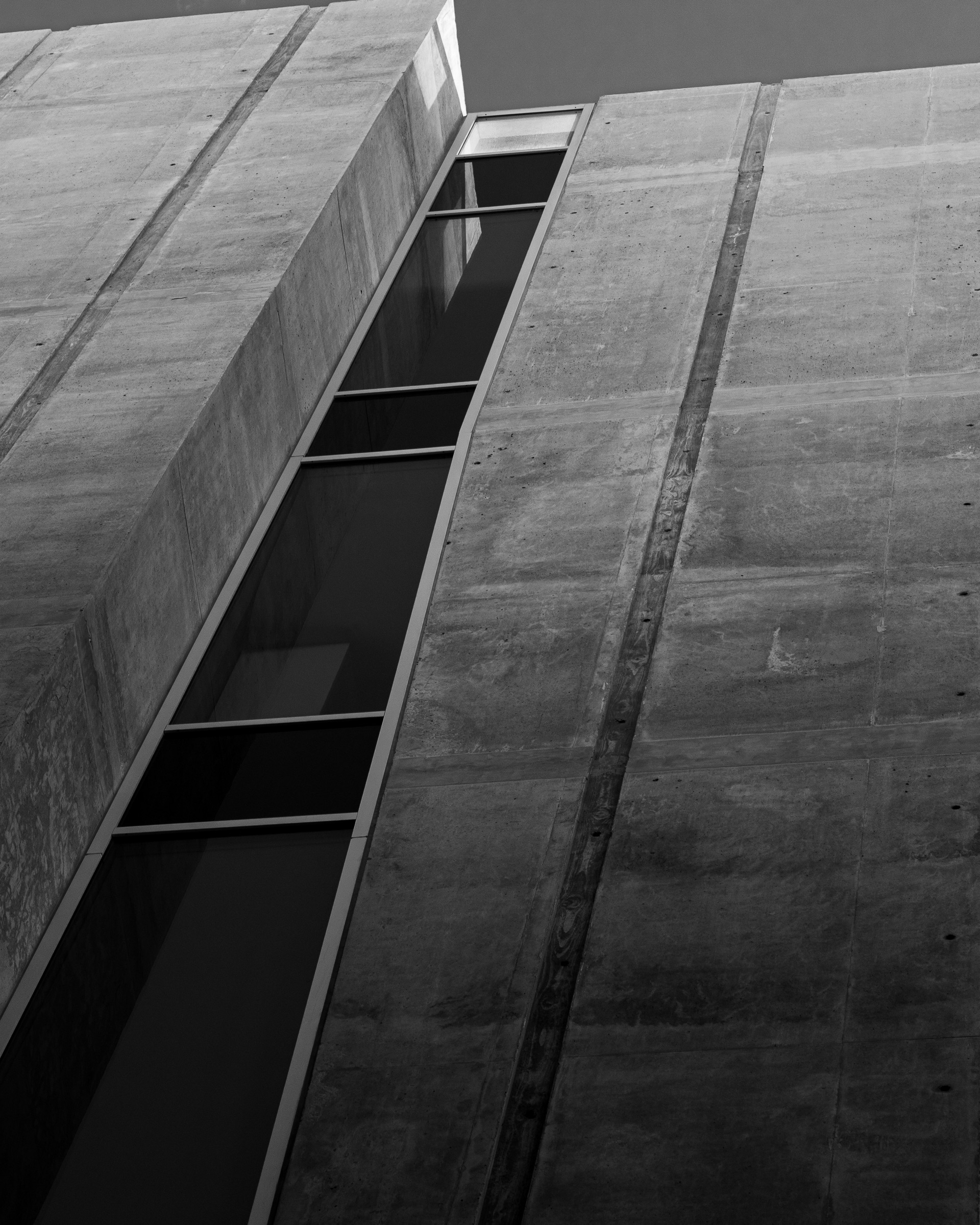 Concrete walls converge around a long dark vertical window